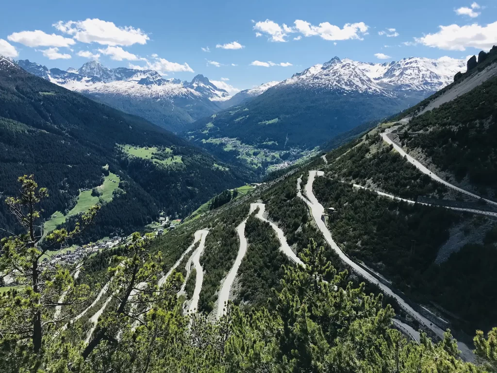 Strada tortuosa di montagna con vista su vallata e montagne innevate.